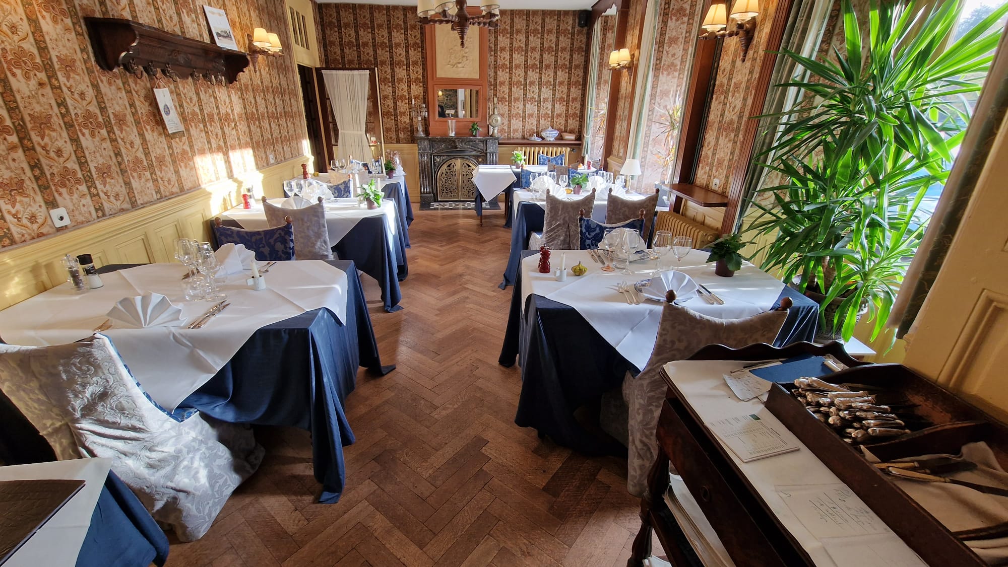 Salle du Restaurant Bonhomme avec tables dressées, nappes bleu et blanc, parquet chevrons et cheminée